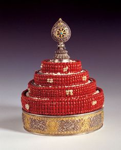 an ornately decorated red and gold box with a silver lid on it's side