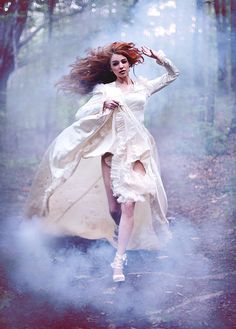 a woman in a white dress is running through the woods with her hair blowing in the wind