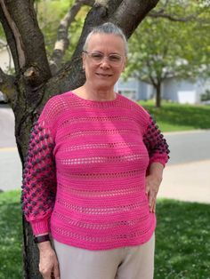 an older woman standing in front of a tree wearing a bright pink knitted sweater