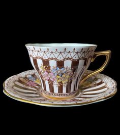 an ornate cup and saucer with gold trimmings on the rim, decorated with flowers