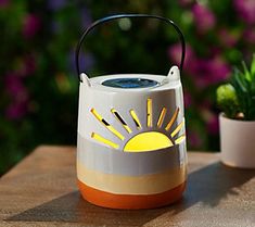 a white and orange lantern sitting on top of a table next to a potted plant