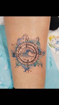 a tattoo on the leg of a person with a compass and wave in blue ink