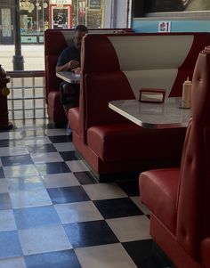 a man sitting at a table in a restaurant with red booths and checkered floor