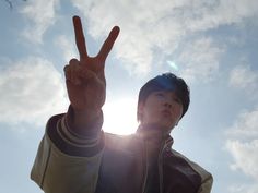 a young man making the peace sign with his hand in front of him, against a blue sky and white clouds