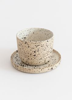 a cup and saucer sitting on top of a white surface with black speckles