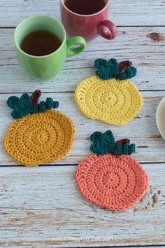 three crocheted coasters sitting on top of a wooden table next to a cup of coffee