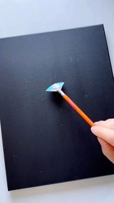 a hand holding an orange and blue toothbrush in front of a black square piece of paper