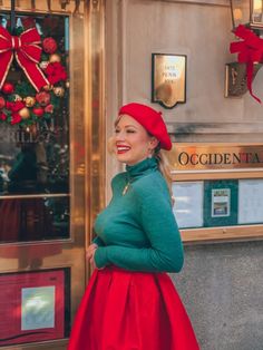 a woman wearing a red hat and green sweater is standing in front of a store