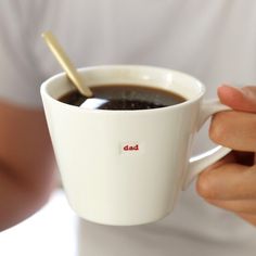 a person holding a cup of coffee with a spoon in it and the word dad on its side