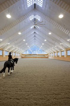 two people riding on the backs of horses in an indoor arena with high ceiling lights