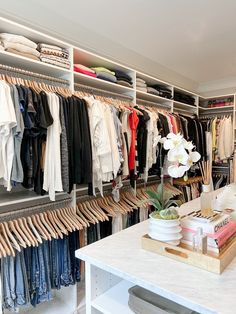 an organized closet with clothes hanging on racks and shelves filled with shirts, pants, sweaters and other items