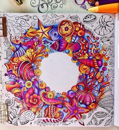 a coloring book with an image of a colorful wreath on the cover and some colored pencils next to it