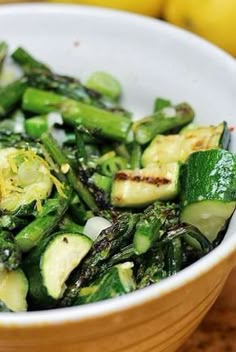 a white bowl filled with green vegetables next to a lemon