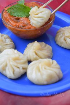 some dumplings on a blue plate with a bowl of sauce