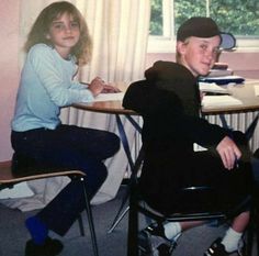 two young children sitting at desks in front of a window, one boy is smiling