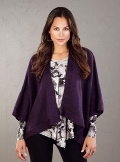 a woman standing in front of a gray wall wearing a purple sweater and black leggings