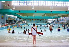 a woman standing in the middle of a swimming pool holding a life jacket and paddle