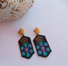 a pair of beaded earrings sitting on top of a white table next to a potted plant