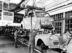 two men working on an old car in a factory