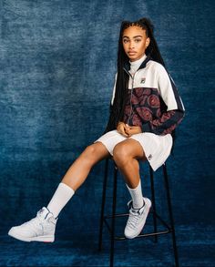 a young woman sitting on top of a chair wearing white tennis shoes and an adidas jacket