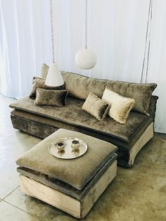 a living room with a couch, ottoman and lamp hanging from the ceiling above it