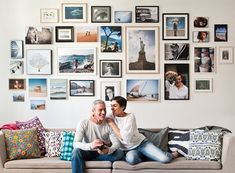 two men sitting on a couch in front of a wall full of pictures