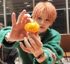 a person holding an orange in front of their face with both hands and wearing a green sweater