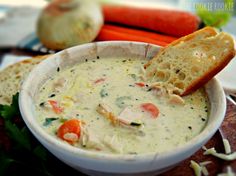 a white bowl filled with soup next to carrots and bread on a cutting board