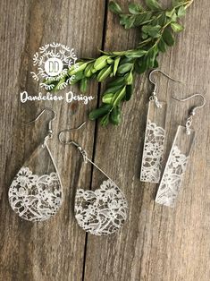 three pairs of white lace earrings sitting on top of a wooden table next to green leaves