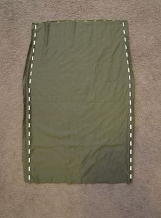 a green skirt with white stitching on the bottom and side, laying on carpet