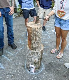 several people standing around a tree stump with an ax in it's center,