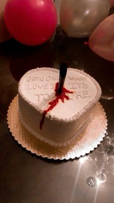 a heart shaped cake with a knife sticking out of it's center surrounded by balloons