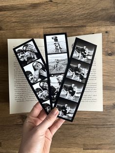 someone is holding three photos in front of an open book on a wooden table with wood grain flooring