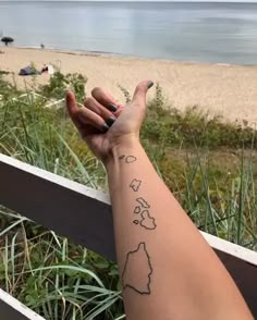 a woman's arm with a small tattoo on it, and the beach in the background