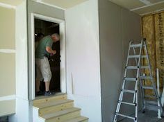 a man standing in the doorway of a house under construction with ladders on each side