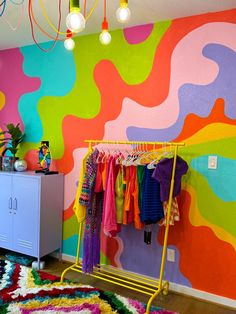 a colorful room with clothes hanging on racks and rugs in front of the wall