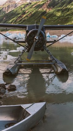 an airplane sitting on top of a body of water next to a boat and mountains