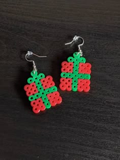 a pair of red and green earrings on top of a wooden table with black background