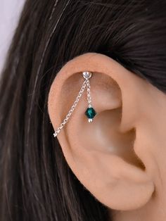 a woman's ear with a chain attached to it and an emerald stone dangling from the side