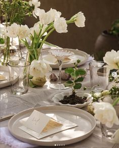 the table is set with white flowers and place settings