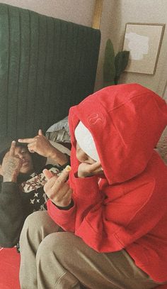 two people in red hoodies sitting on a couch with one pointing at the camera