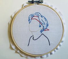 a hand embroidered portrait of a woman's face in blue and red on a white background