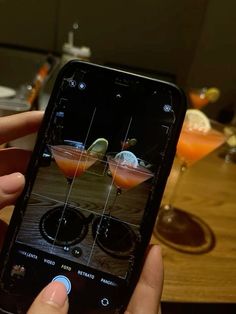 a person holding an iphone taking a photo of cocktails