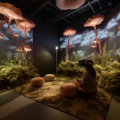 a woman is sitting on the ground in front of an aquarium with mushrooms and other plants