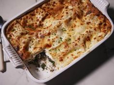 a casserole dish with cheese and spinach in it next to a spoon