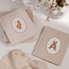 three books with teddy bears on them sitting next to a white vase and flower arrangement