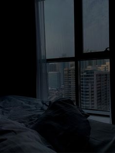 a bed in a dark room next to a large window with city lights on it