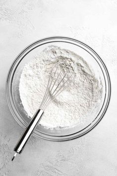 a bowl filled with flour and whisk on top of a white countertop