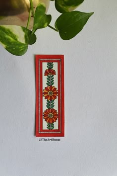 an orange and yellow flower on a white wall next to a green leafy plant