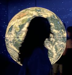 a woman standing in front of a large circular object with the earth on it's side